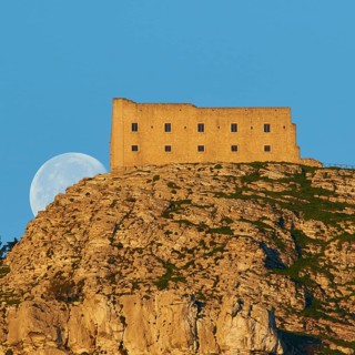 Morning light, super clear blue sky, huge full moon, sets behind mountain, fortress-like building