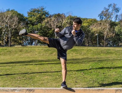 Young athletic martial arts fighter practicing kicks in a public park