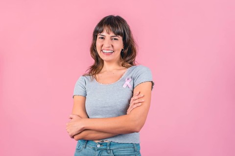 Happy woman wearing a pink breast cancer awareness ribbon while looking at camera