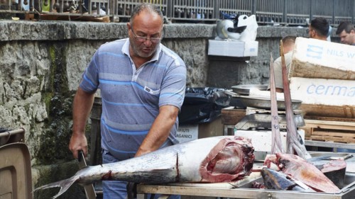 Vendor cuts up huge tuna with a cleaver, fish market, old town, Catania, east coast, Sicily, Italy,