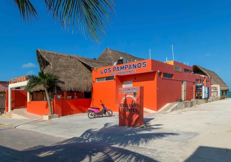 Thatched palapa roofed buildings and bright orange exterior of Los Pampanos seaside restaurant,