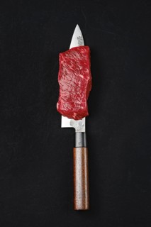 Piece of raw strip steak on the blade of knife