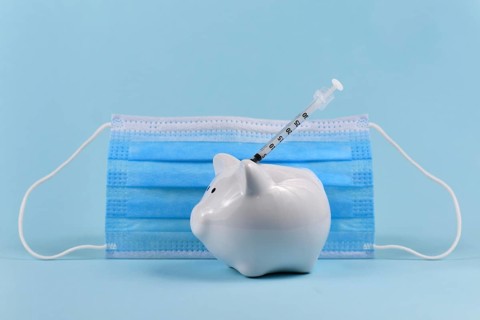 Corona virus vaccine expenses concept with white piggy bank, syringe and medical face mask on blue
