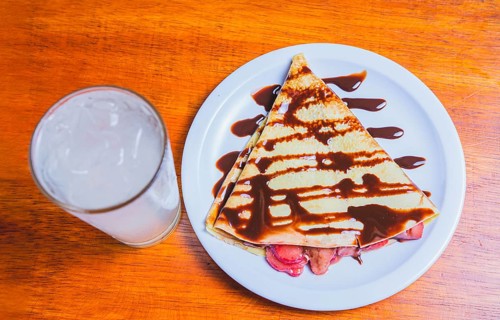 Crepe with chocolate cream and strawberry with drink on the table. Sweet strawberry crepe with