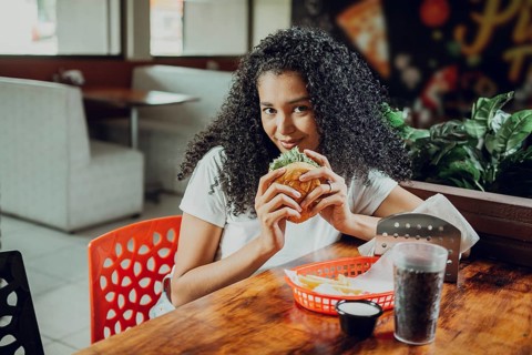 Portrait of afro girl holding a hamburger in a restaurant. Beautiful latin girl enjoying a