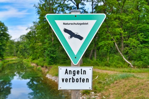 German sign for German Nature Reserve and no fishing sign in front of river