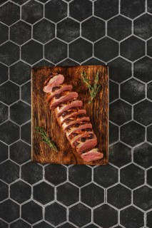 Overhead view of a seared duck breast cut on slices on wooden chopping board