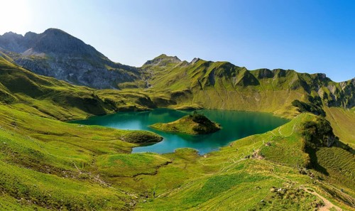 Schrecksee in the midst of green mountains under a clear sky, surrounded by lush vegetation and a