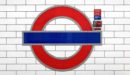 A well-known round tube sign in red and blue on a white tiled wall of a railway station, London,