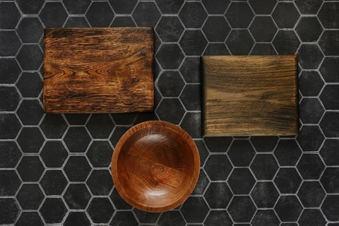 Top view of empty round wooden bowl and cutting boards on a black hexagonal tiled background