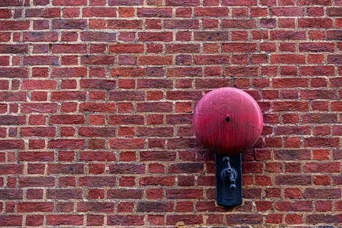Close-up of a red brick wall with a red alarm bell