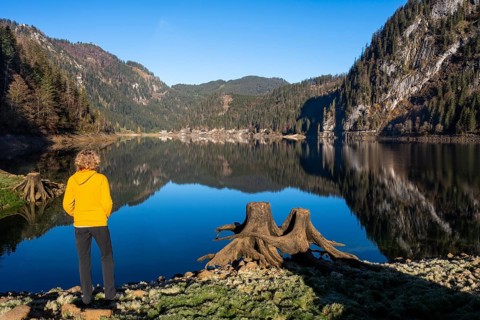 The Vordere Gosausee in autumn with a view of the Gasthof Gosausee. A hiker stands by the lake. Two