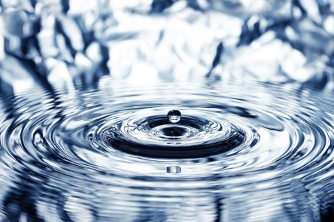 A drop of water falls onto the water surface and creates concentric circles, waves, rings