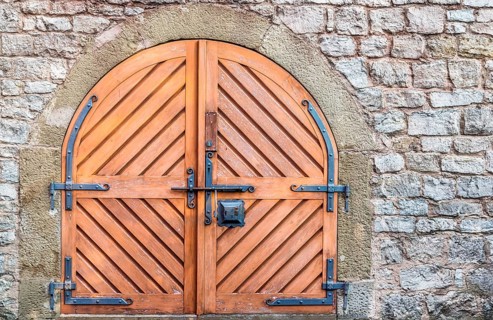 Ancient wooden door with metal hinged and latch, on a weathered stone wall