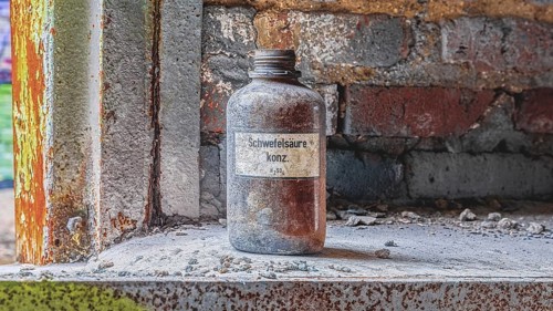 An obsolete sulphuric acid bottle stands on a dusty windowsill in an industrial setting,