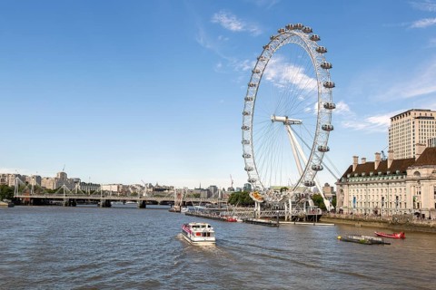 The Thames with boats and the London Eye Ferris wheel under a blue sky in London, United Kingdom,