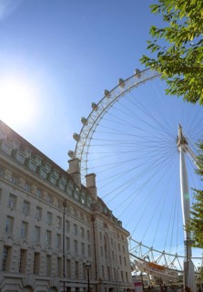 The London Eye Ferris wheel next to an old building under a blue sky with rays of sunshine, London,