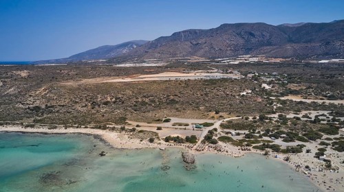 Overtourism, A beach with clear water, surrounded by a wide, dry landscape and mountains in the