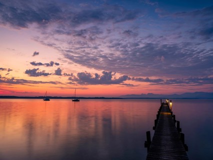 Sailing boats and jetty on Lake Chiemsee at dawn, with the Chiemgau Alps in the background,