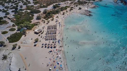 Overtourism, aerial view of a beach with people and umbrellas and a roof area next to the water,