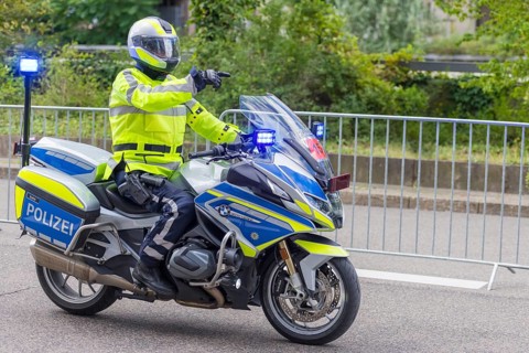 A policeman in a high-visibility waistcoat rides a police motorbike with blue lights and shows the