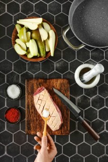Top view of hand adding salt on raw duck breast with the skin cut crosswise on wooden chopping
