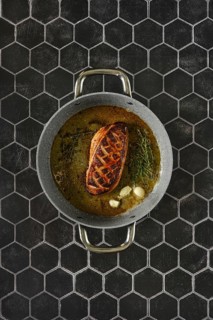 Top view of a perfectly seared duck breast with fresh thyme and garlic in a cooking pan