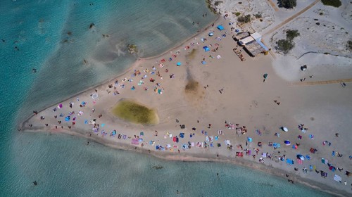 Overtourism, aerial view of a beach with many people and colourful umbrellas enjoying the sand and