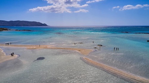 Clear blue sea with sandbanks and an island in the background. Few people enjoy the quiet