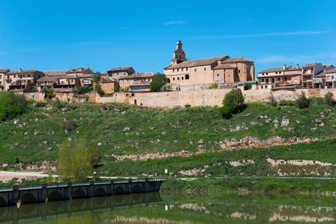 Historic town with church on a hill above a river with a stone bridge, the water reflects the