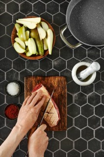 A chef skillfully slices criss-cross a juicy piece of duck breast fat on a rustic wooden cutting