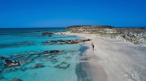 A person walks on the sandy, rocky shore along the clear blue sea. Quiet and unspoilt nature,