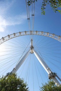 Close-up of the London Eye Ferris wheel and structure with trees and blue sky in the background,