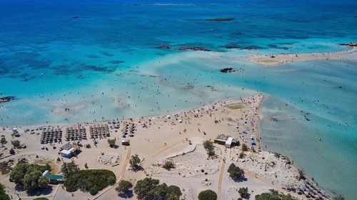 Overtourism, aerial view of a beach with people and umbrellas surrounded by blue sea water,