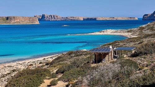 Caretaker building, coastal landscape with blue water, solar panels and green hills, quiet beach,