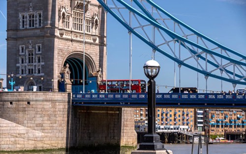 Part of Tower Bridge with the River Thames below and red bus in the background, illuminated by