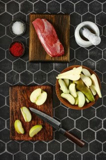 Overhead view of sliced apples and pears laid out on a chopping board next to the duck breast