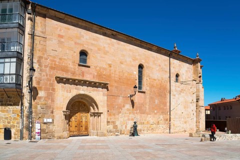 A simple historic church with a sandstone-coloured façade and large doors in an empty square under