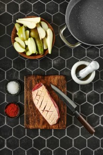 Overhead view of raw duck breast with the skin cut crosswise on wooden chopping board surrounded
