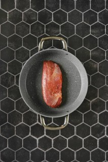 Top view of a raw duck breast lying on a non-stick pan with two handles, against a background of
