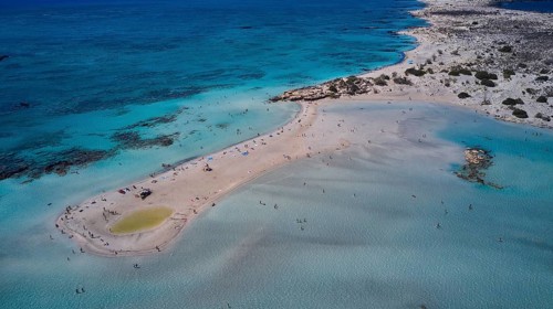 Overtourism, aerial view of a sandy beach with people in the shallow, clear water of the sea,