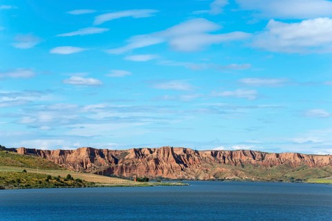 A clear blue lake surrounded by majestic rock formations and rolling hills under an expansive sky,