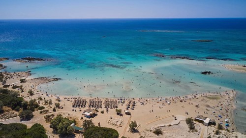Overtourism, sandy beach with many parasols and people enjoying the clear blue sea. The sky is