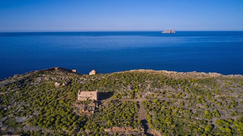 Drone shot, ruins on cliffs by the sea with sweeping views and lush vegetation to the horizon,