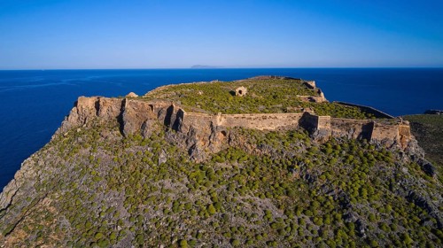 Drone shot, An old fortress perched on a green, rocky hill with sweeping sea views and surrounding
