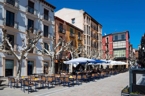 An empty sidewalk café along a row of buildings in clear, sunny weather with blue umbrellas and