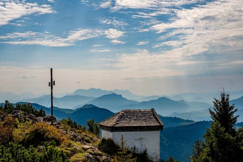 Summit cross and chapel of the Spitzstein, behind the silhouettes of the Loferer and Chiemgau Alps,
