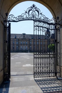 Iron gate opens onto a sunny courtyard with historic building, Echternach Abbey, Echternach,
