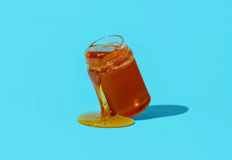 Jar with honey minimalist on a blue table. Dripping honey from a glass jar directly on the table