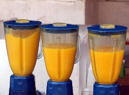 Three electric blenders are making fresh mango smoothies